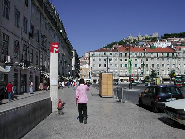Man in pink shirt walking toward Praça da Figueira, Lisbon, São Jorge Castle on the hill