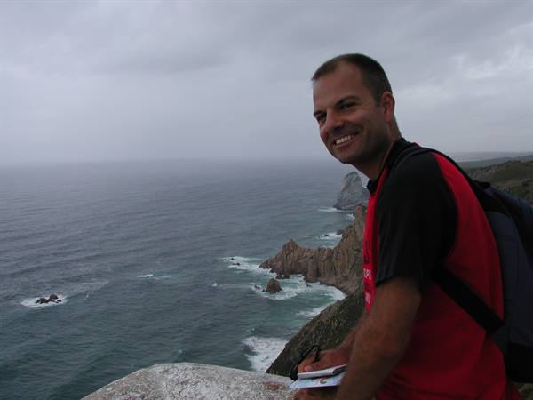 Smiling tourist with backpack and map on ocean cliffs at Cabo da Roca