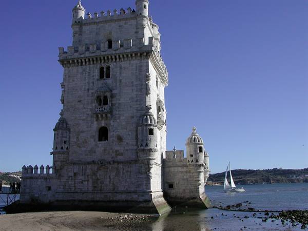 Belém Tower in stone by the Tagus River, a sailboat passing nearby