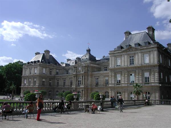 Tourists seated in front of the Luxembourg Palace in Paris, pale stone under cloudy sky