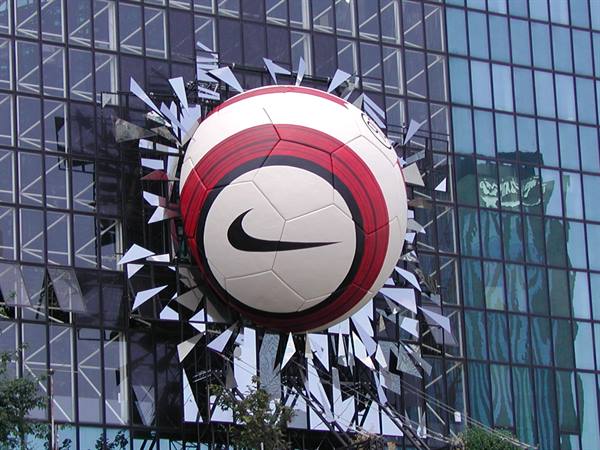 Giant Nike soccer ball crashing through a glass skyscraper facade