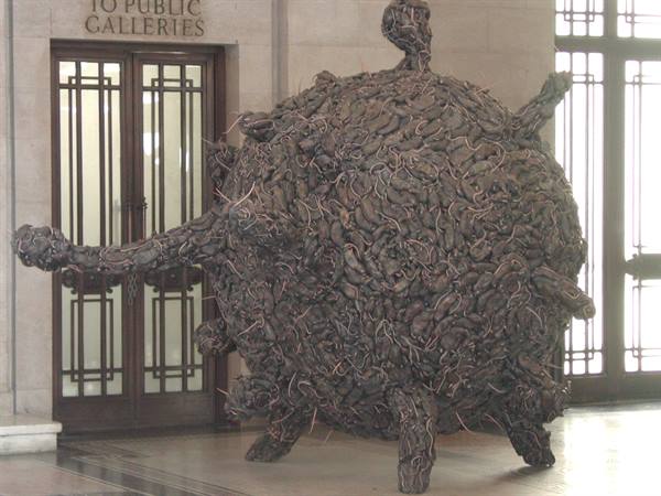 Spiky brown sphere sculpture installed inside an art gallery with wooden door