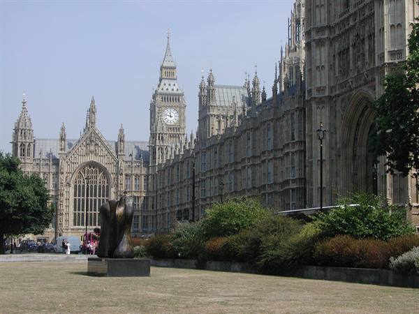 Clock tower and Gothic facade of the Palace of Westminster, bronze statue on the lawn