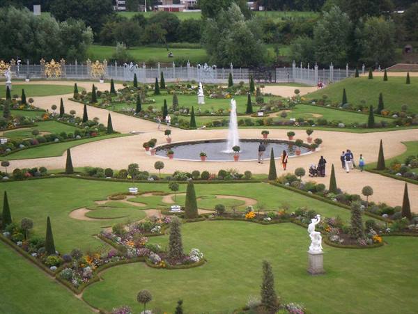 Formal garden with central fountain, clipped hedges and statues, visitors on gravel paths