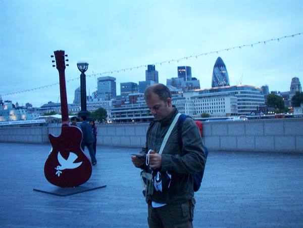 Man checks his phone beside a red guitar sculpture with dove, London's Gherkin behind