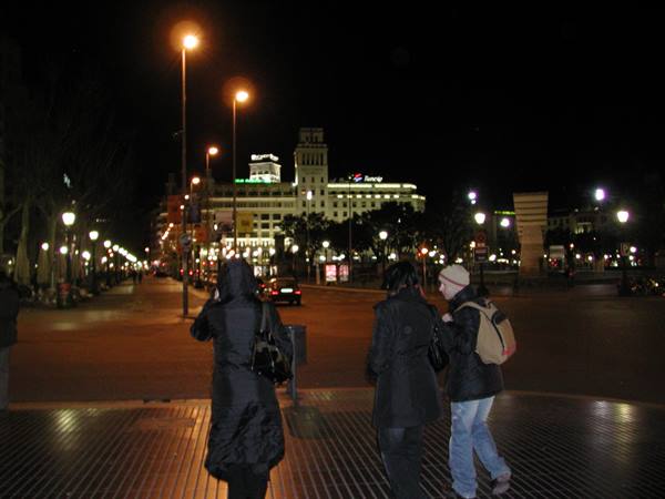 Pedestrians in hoods crossing Plaça de Catalunya, Barcelona, at night
