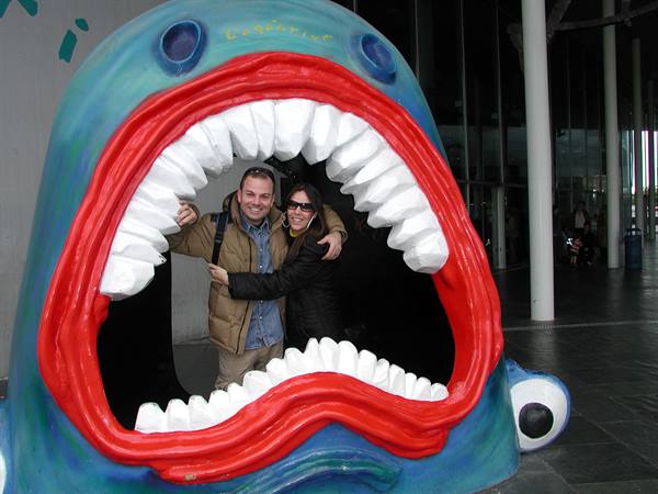 Couple hugging inside the toothy mouth of a blue sculpture