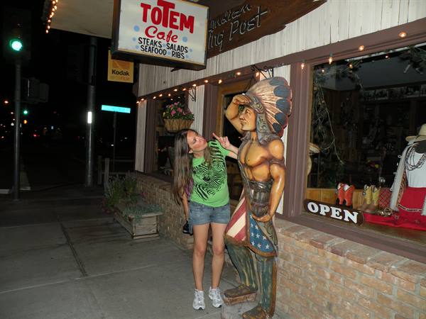Girl next to the wooden cigar-store Indian statue outside Totem Cafe