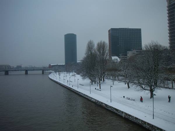 Snowy riverside promenade along the Main, skyscrapers in the fog