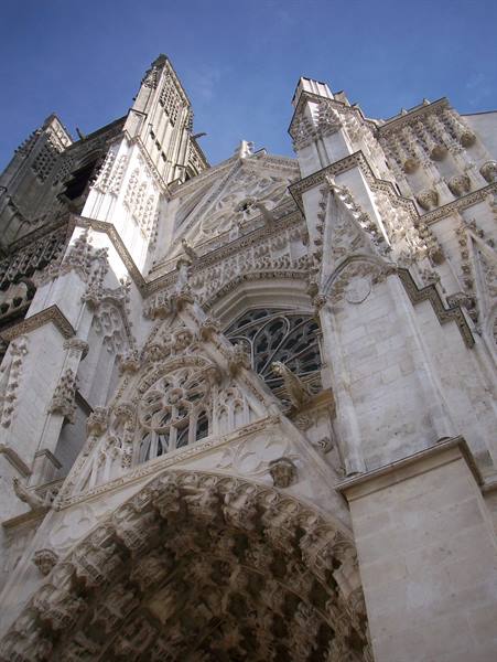 Gothic cathedral in pale stone, carved spires and portals against a blue sky