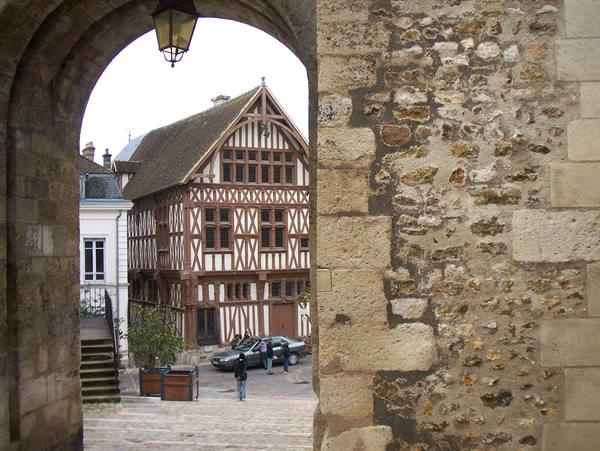 Half-timbered house seen through a medieval stone archway