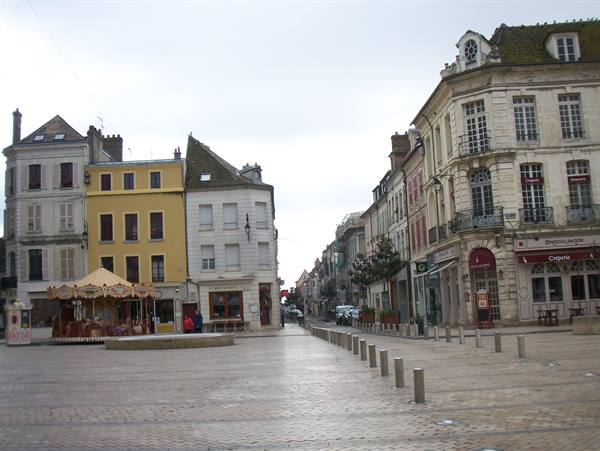 Square with wooden carousel, colorful old buildings, wet cobblestones under grey sky