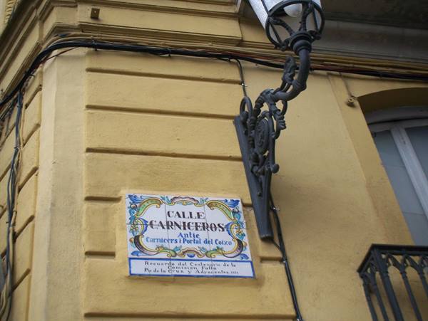 Ceramic street sign Calle Carniceros on yellow wall, wrought iron lamp