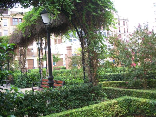 Wooden and iron bench under a green pergola with black lantern in a city garden