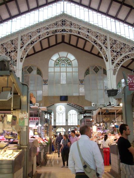 Shoppers among market stalls under iron arches and stained glass windows