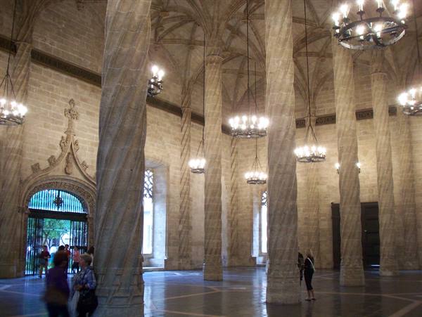 Spiral stone columns in Valencia's Silk Exchange, lit chandeliers, visitors walking