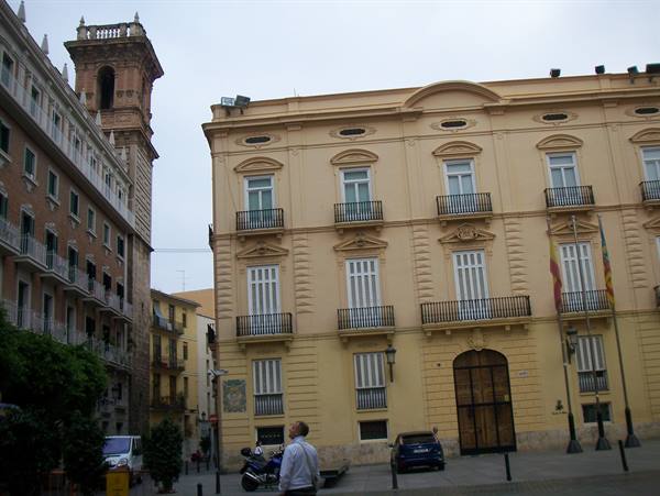 Man gazes at yellow palace with balconies and flags in Valencia