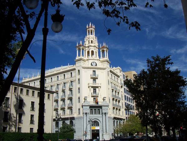 White building with clock tower framed by branches and a street lamp, Málaga