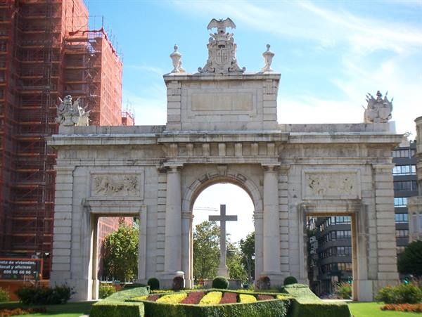 Monumental stone gate with carved arches in Madrid, a cross behind