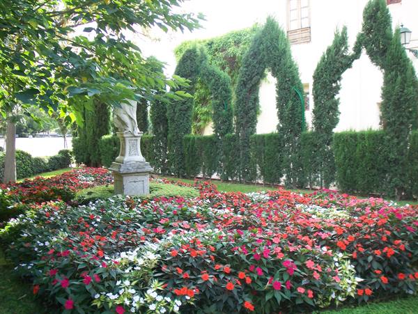 Marble statue among red and white flowerbeds, cypress trees carved into arches