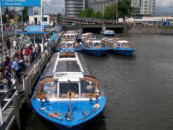 Blue glass tourist boats moored at a busy dock in Amsterdam