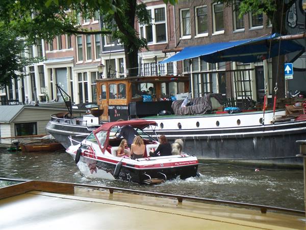 Red and white motorboat cruising an Amsterdam canal past houseboats and brick houses