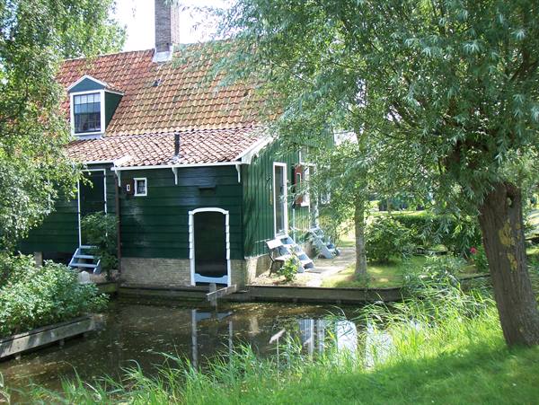Green wooden house with tiled roof reflected in the water, Zaanse Schans