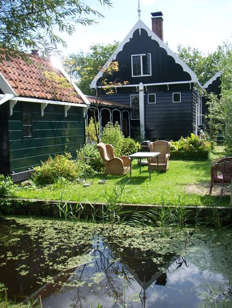Black wooden houses by a canal, wicker chairs on the green lawn