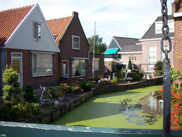 Brick houses along a green canal, drawbridge chain in the foreground
