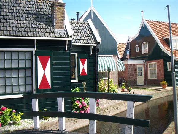 Green wooden houses with red shutters, bridge and canal in Marken