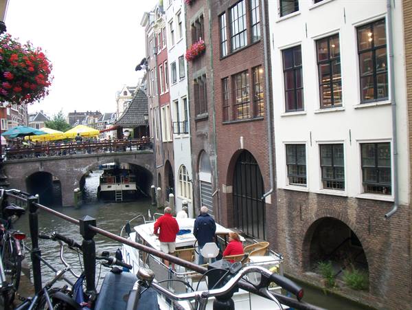 Boats along Utrecht canal, brick houses, bicycles and a bridge with umbrellas