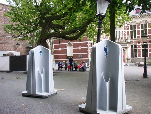 White public urinals on a cobbled square with people sitting near the buildings