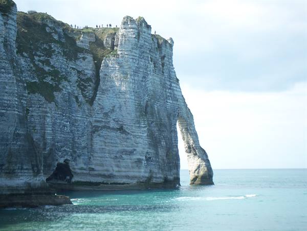White chalk cliff with natural arch at Étretat, tourists on top, turquoise sea