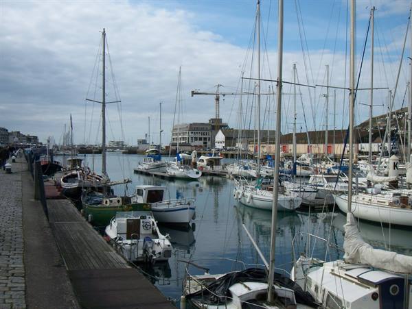 Sailboats moored in the harbor beside a stone pier under cloudy sky