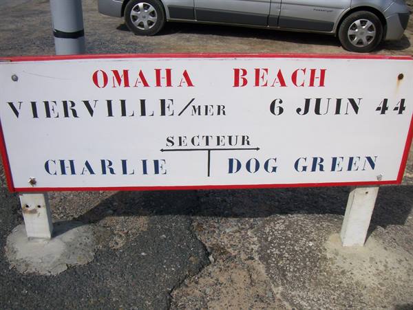 White Omaha Beach sign with red and blue lettering, car parked behind