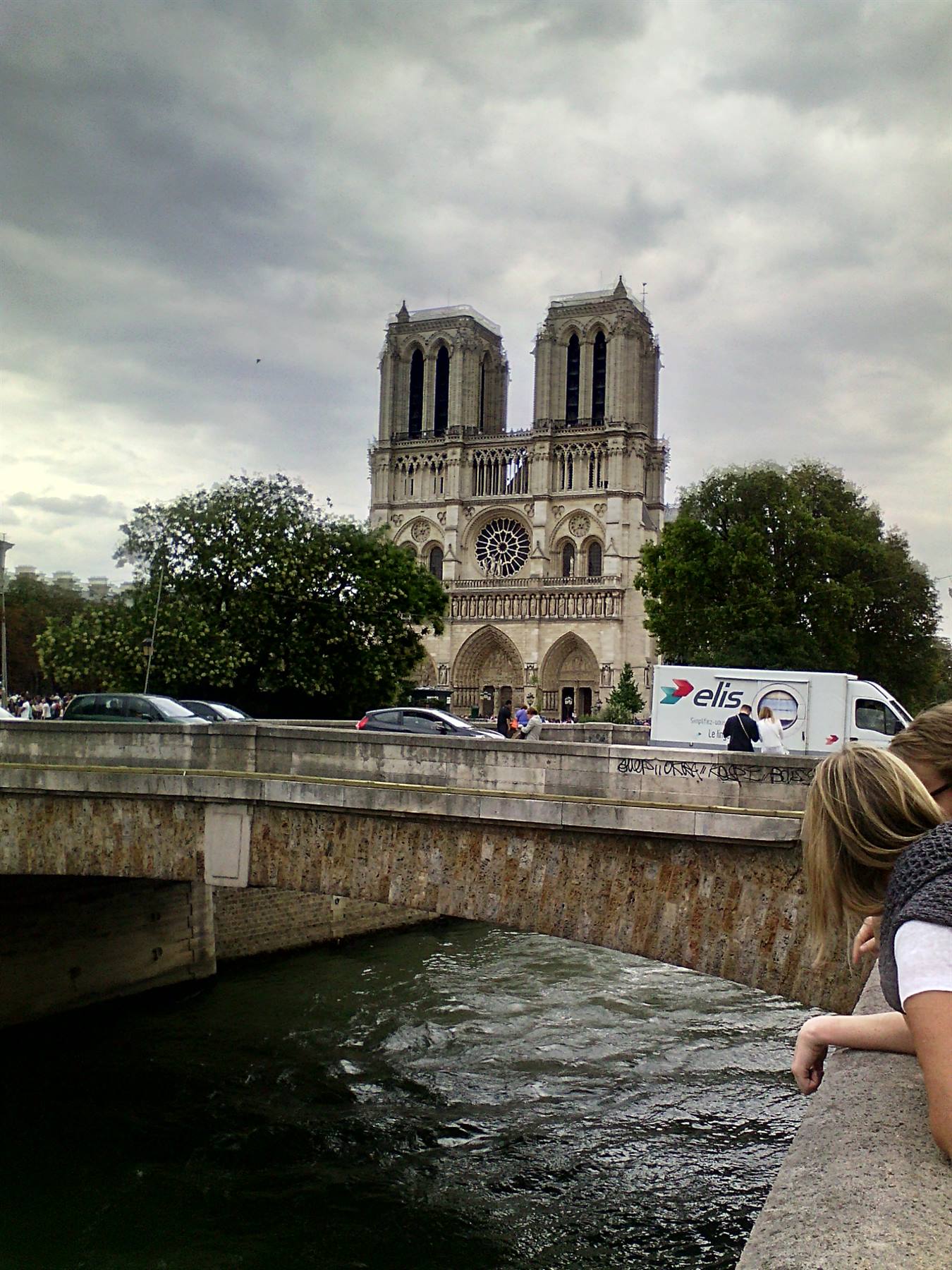 Turiste sul ponte sulla Senna guardano la facciata gotica di Notre-Dame sotto cielo grigio