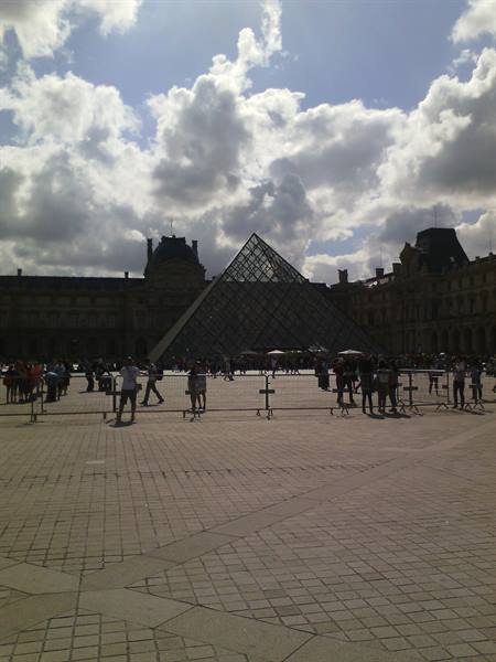 Glass Louvre pyramid under clouds, tourists in the Paris courtyard