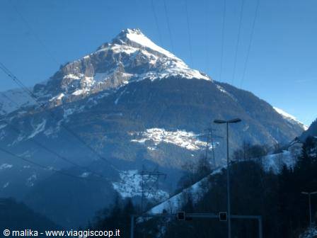 Snow-capped mountain under blue sky, power lines and streetlights in foreground
