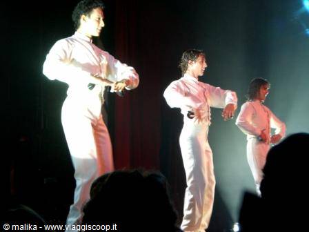 Dancers in white suits perform in line under stage lights