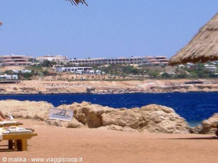 Straw umbrellas and sunbeds on sandy beach, resorts along rocky blue coastline