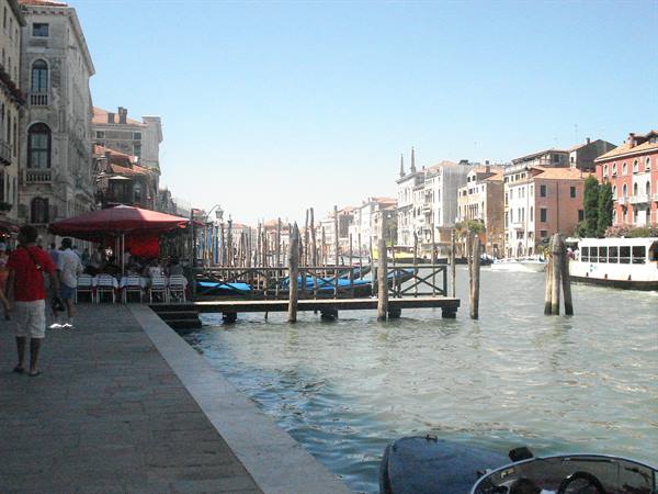 Wooden dock on Venice Grand Canal, mooring poles and vaporetto under sunny sky