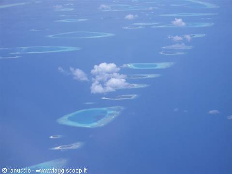 Turquoise coral atolls among white clouds, photographed from the airplane over the Indian Ocean