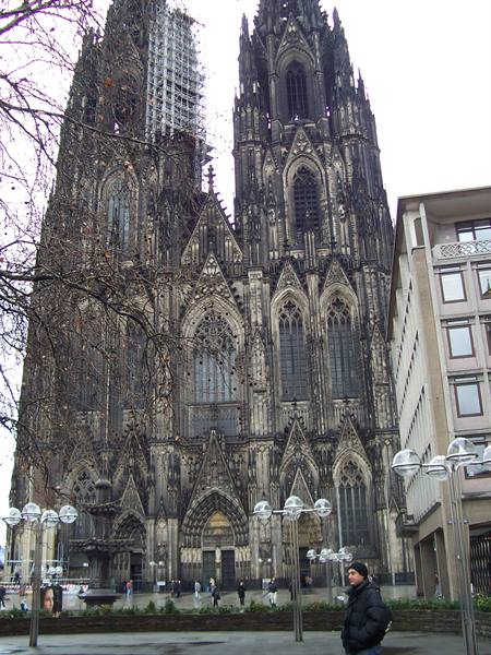 Man in black jacket in front of Cologne Cathedral's dark Gothic stone facade