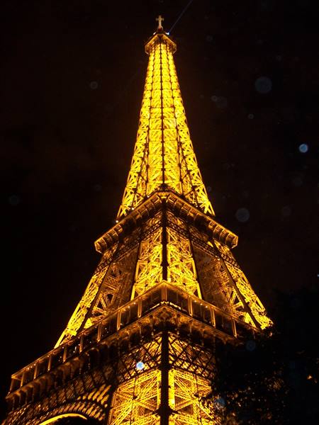 The Eiffel Tower iron lattice glowing golden against the dark night sky