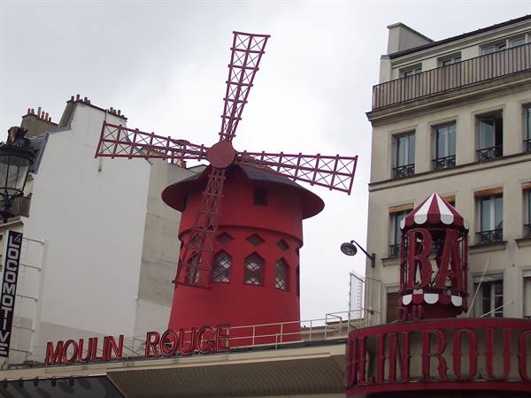 The Moulin Rouge red windmill against a grey sky, Parisian buildings nearby