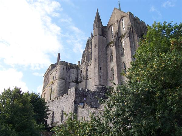 The stone abbey of Mont-Saint-Michel rises above the trees, blue sky