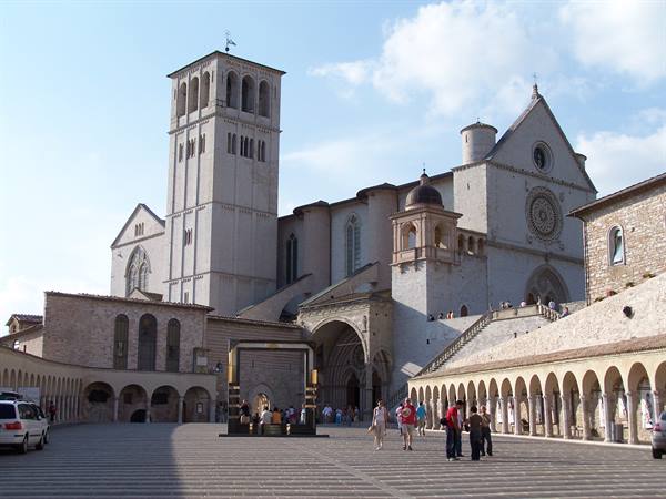 Basilica of Saint Francis in Assisi, sunny square with visitors and stone arcades