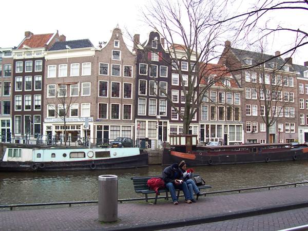 Couple sitting on a bench along an Amsterdam canal with houses and houseboats