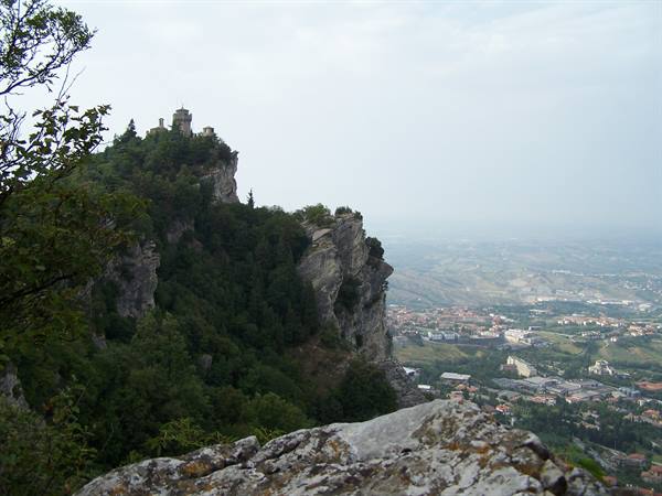 San Marino tower atop the cliff, green trees, town in hills below
