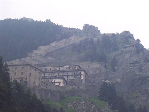 Fenestrelle Fort in the mist, stone walls climbing the mountain among firs
